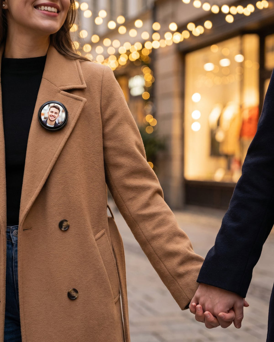 Woman in a camel coat holding hands on a lit street, her Lumipin showing her partner.