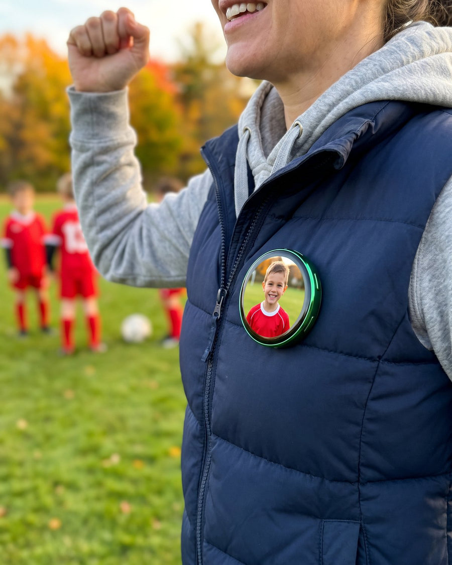 Mom cheering at a youth soccer game, her green Lumipin showing her son in a red jersey.