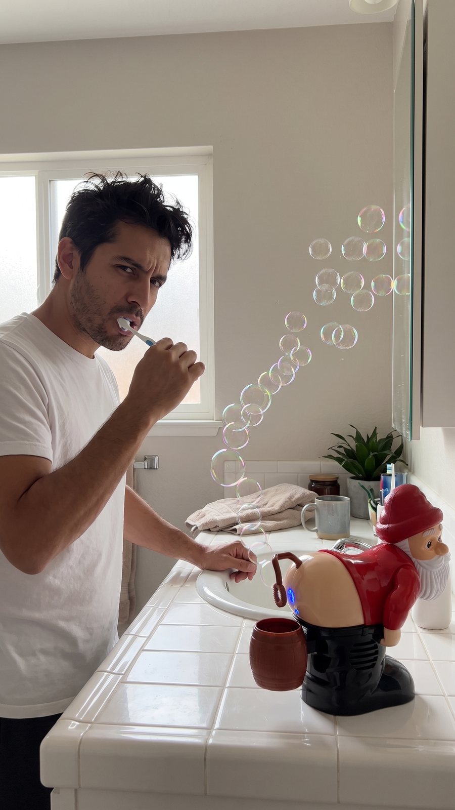 A dad brushing his teeth stares down at the Santa on the bathroom counter as bubbles drift at his face.